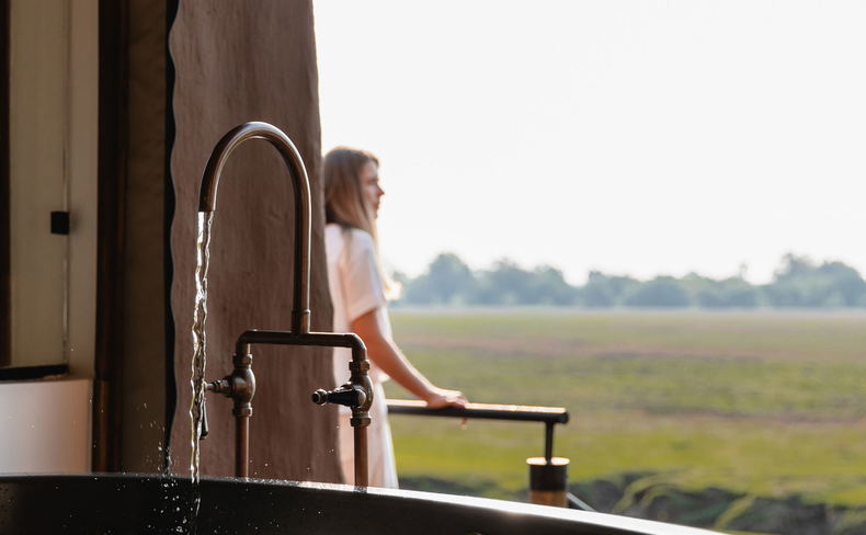 lady guest on deck with bath running in foreground at Puku Ridge Camp Zambia Luangwa Plains lady guest on deck with bath running in foreground at Puku Ridge Camp Zambia Luangwa Plains