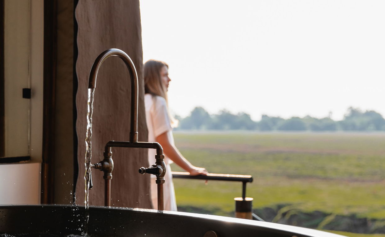lady guest on deck with bath running in foreground at Puku Ridge Camp Zambia Luangwa Plains lady guest on deck with bath running in foreground at Puku Ridge Camp Zambia Luangwa Plains