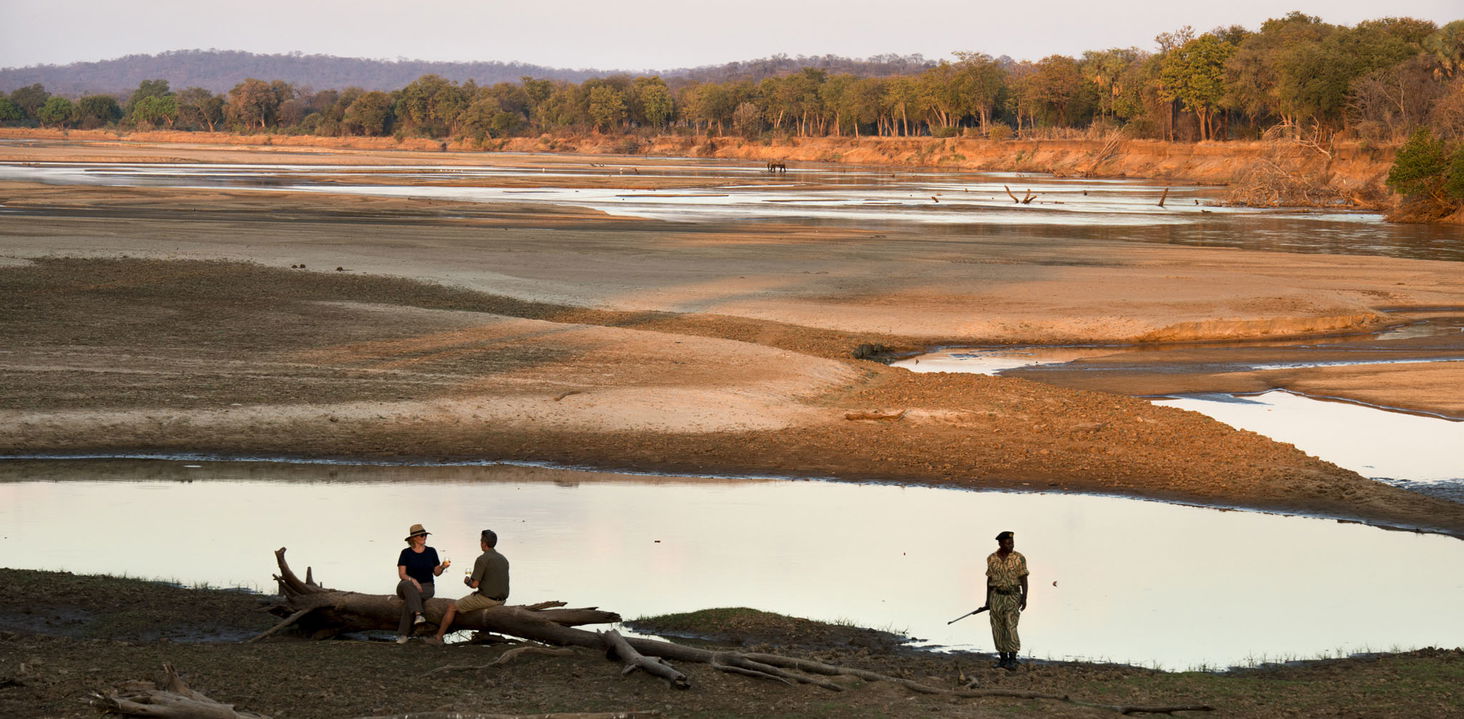 two guest sand guide by river at sunset close to lodge of Puku Ridge Camp Zambia