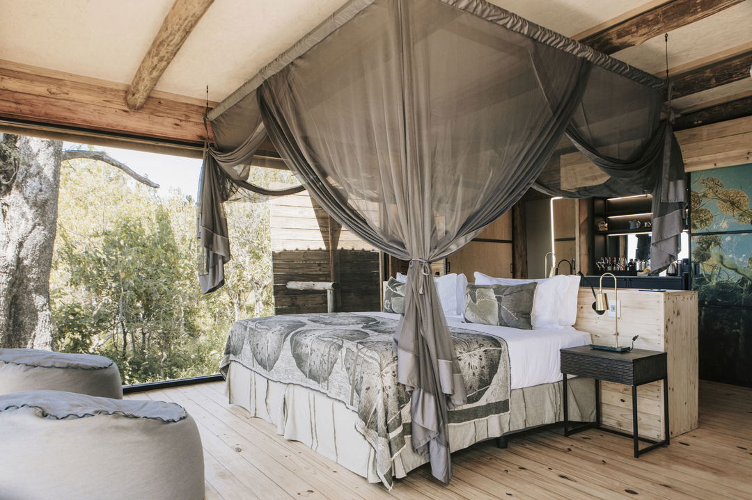 interior of luxury room with double bed and open patio at Vumbura Plains Camp Wilderness Okavango Delta