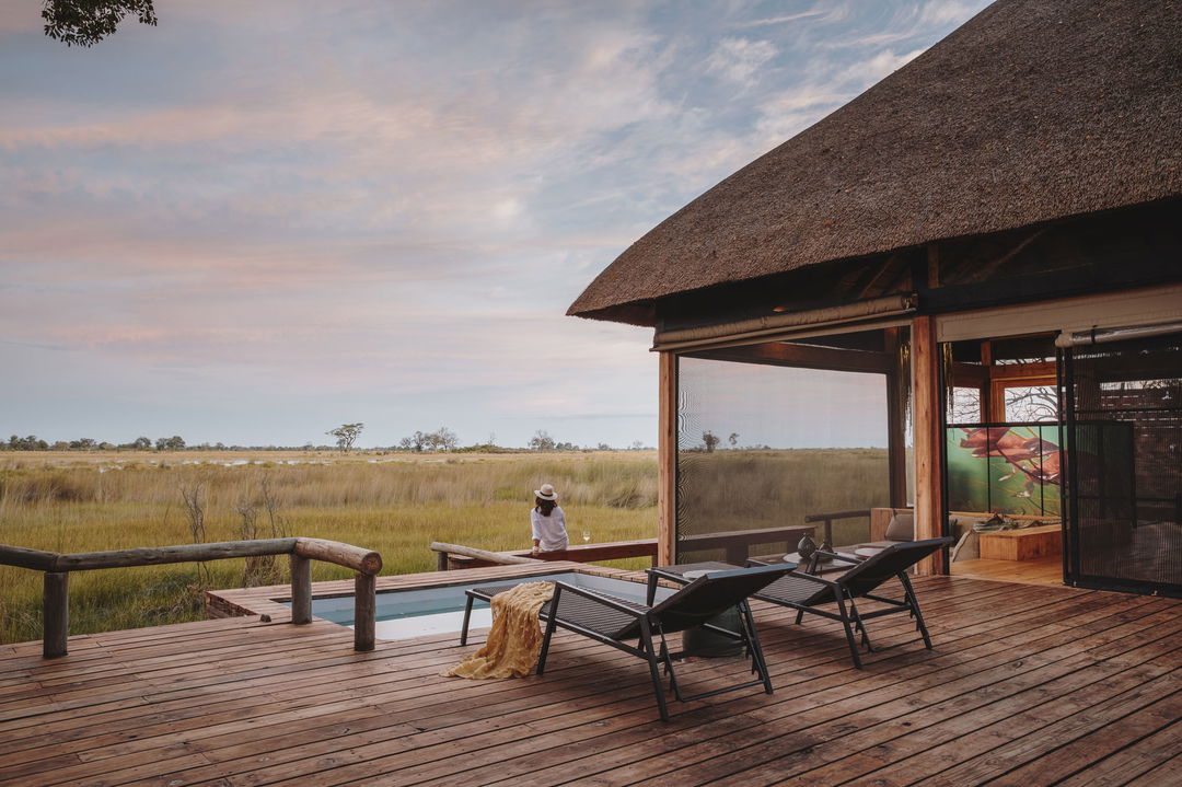 guest and deck chair by pool and views of delta beyond at Vumbura Plains Camp Wilderness Okav