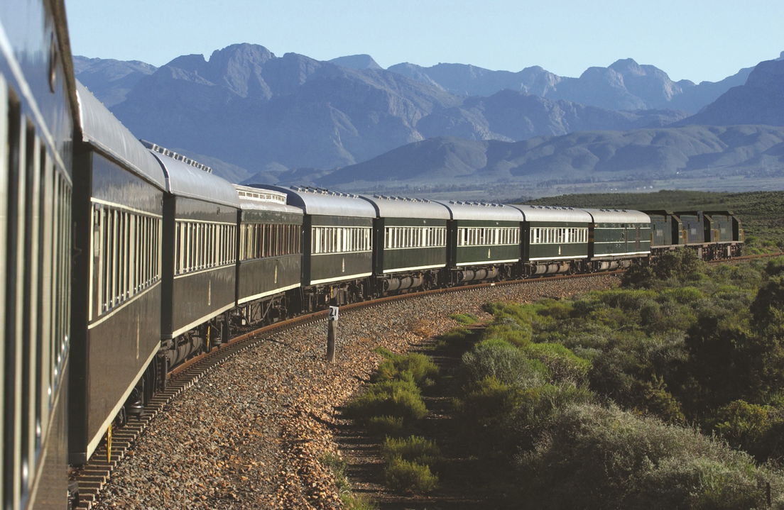 view of train in the cape countryside and mountains in backfrop with rovos rail luxury trains