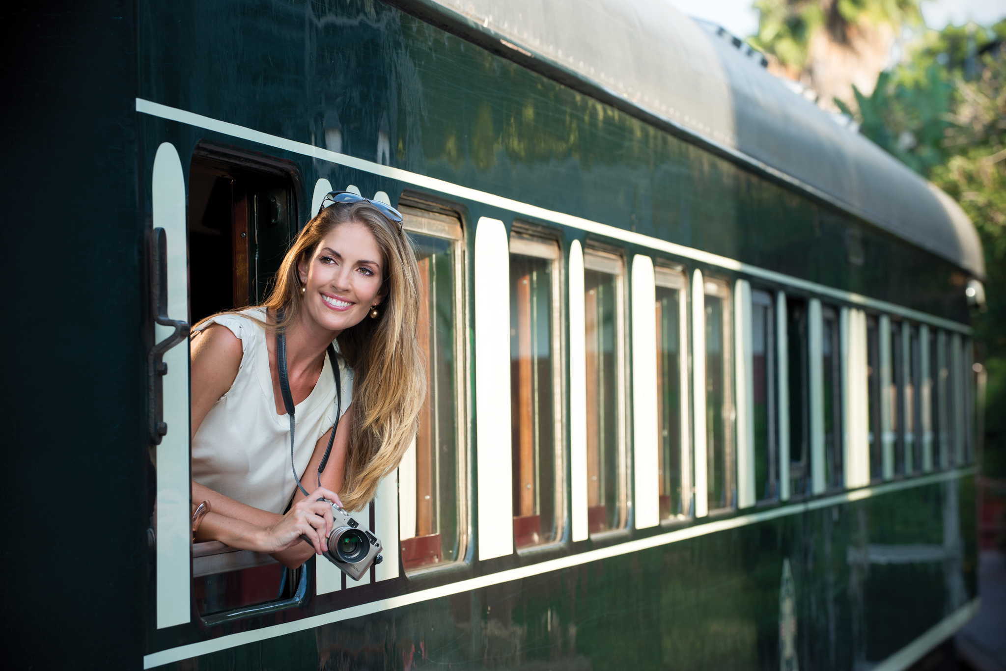 smiling lady with camera looking out from train cart ready to depart at Rovos rail luxury train safaris