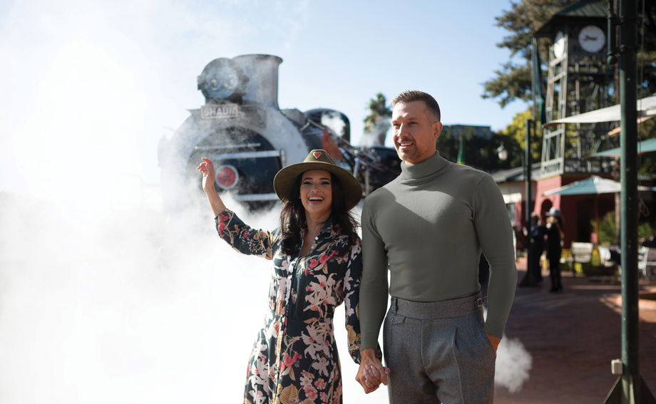couple holding hands on platform of station in front of steam train ready to depart at Rovos rail luxury train safaris