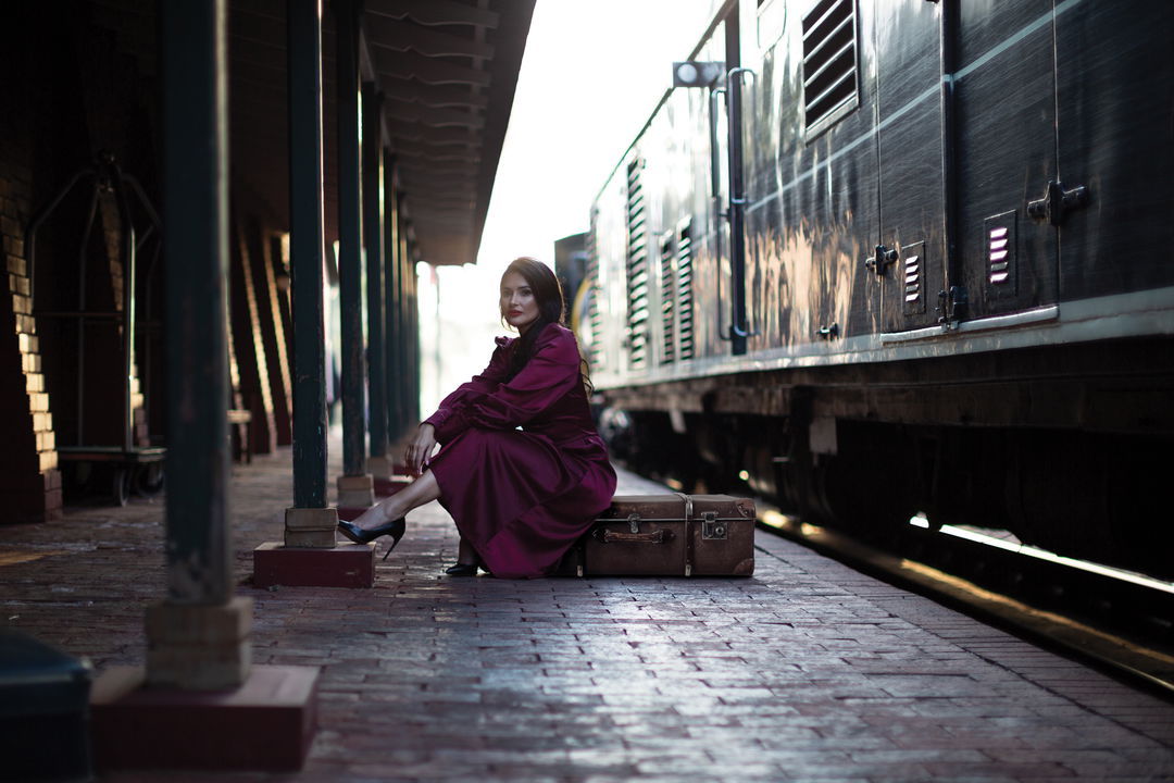 lady guest sitting on luggage next to train on station platform of Rovos Rail Luxury Trains