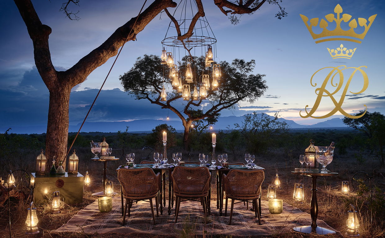 Bush dinner with tables set under tree with lanterns waterside bush lodge Royal Malewane - logo 