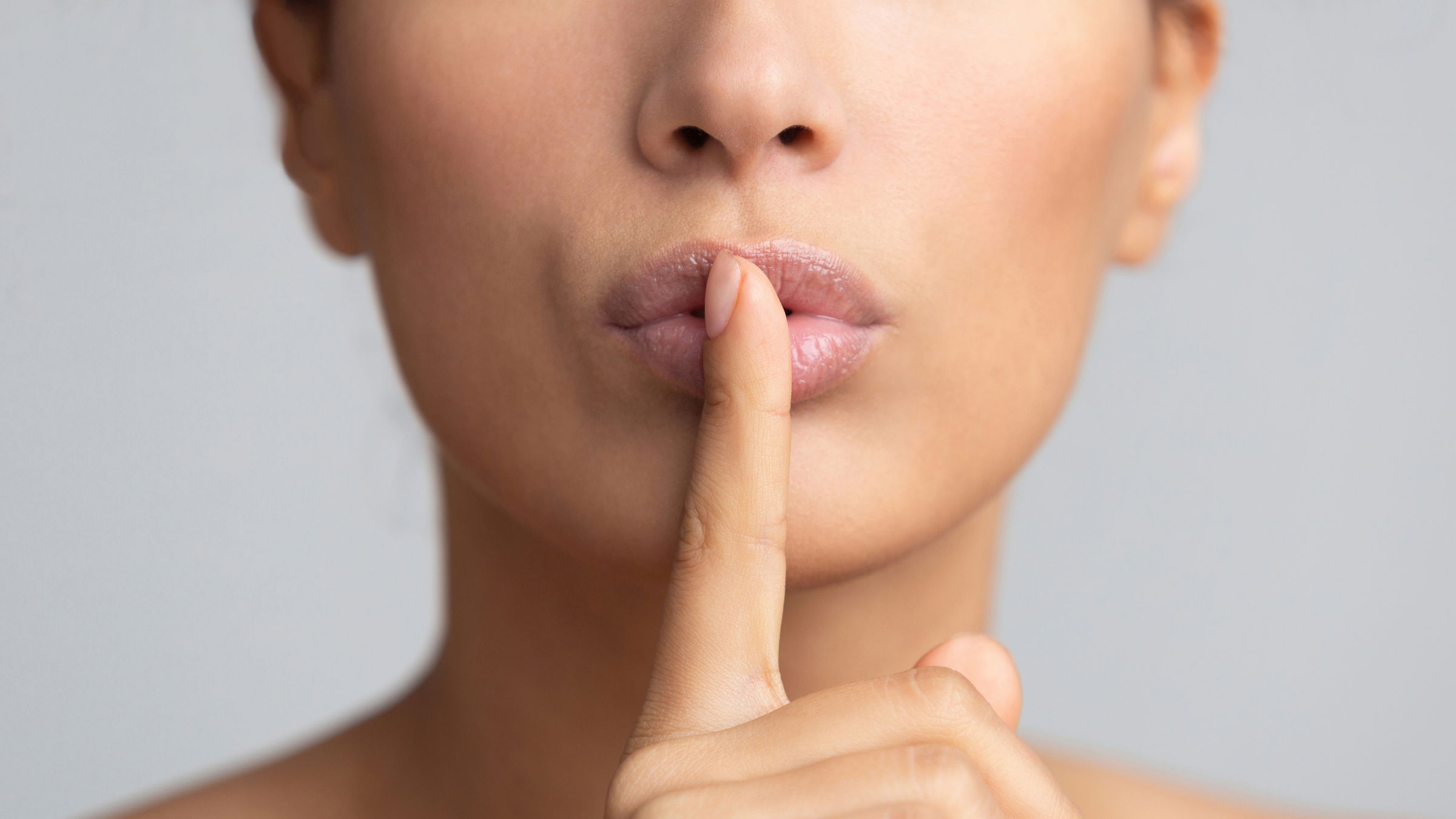woman with finger on lip signalling to keep quiet