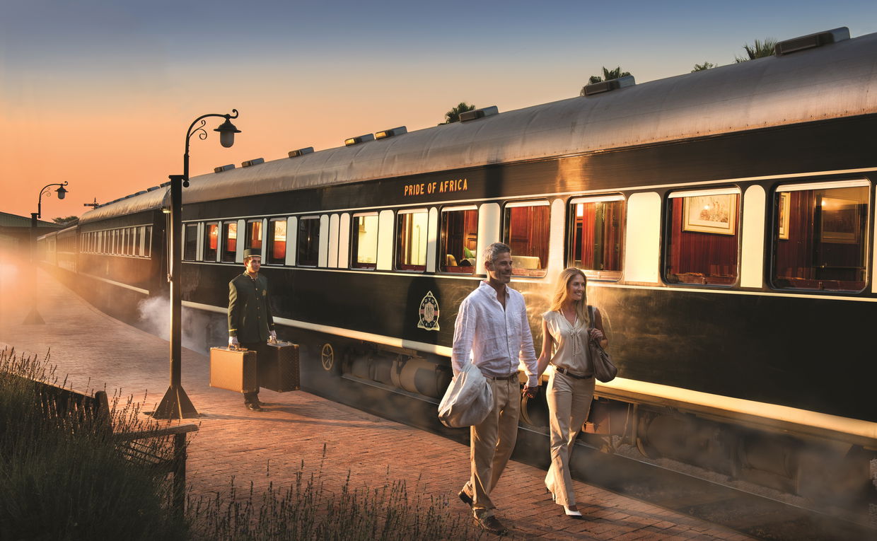 porter with luggage walking behind couple on platform waiting for train to depart at Rovos station