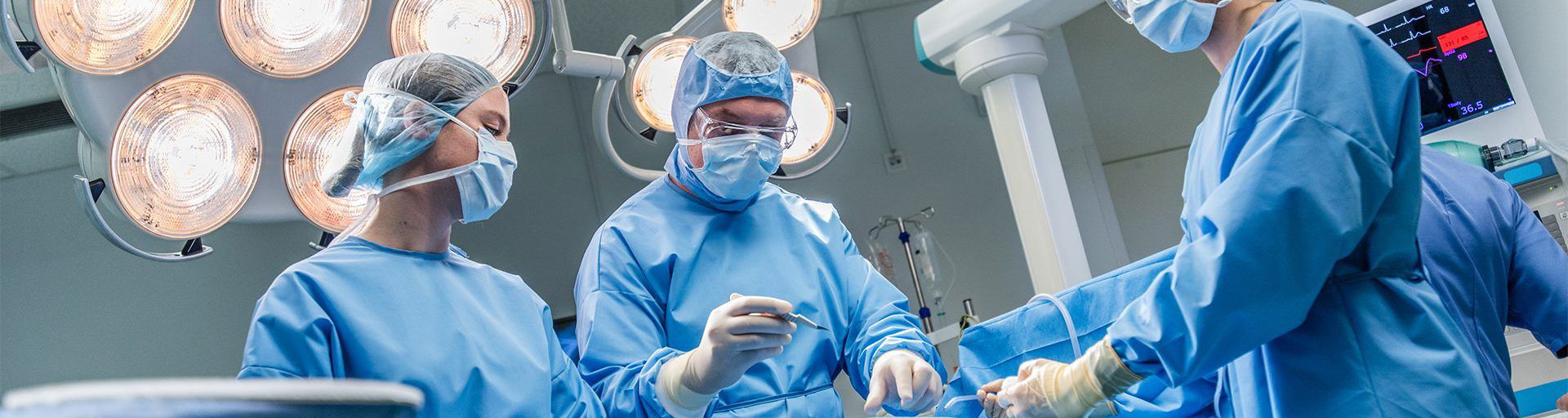 surgeon operating on patient in theater under lights assisted by two doctors