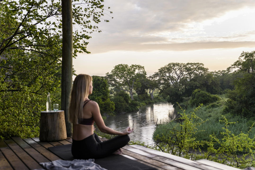 lady doing yoga on deck with river views at Singita Faru Faru lodge Serengeti