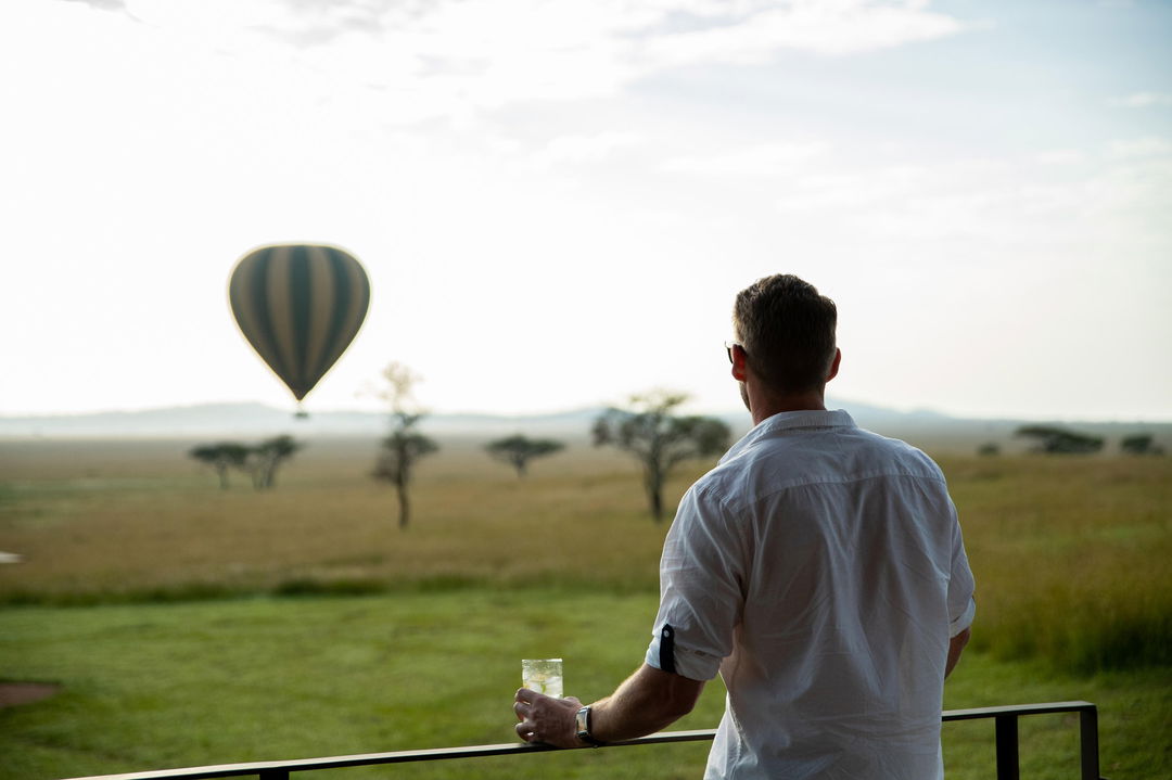 guest on deck of suite at Singita Sasakwa lodge in Serengeti looking at hot air balloon beyond