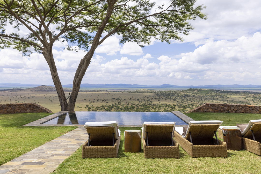 loungers by splash pool of suite overlooking plains of lady guest in the main rim pool of Singita Sasakwa lodge overlooking the Serengeti