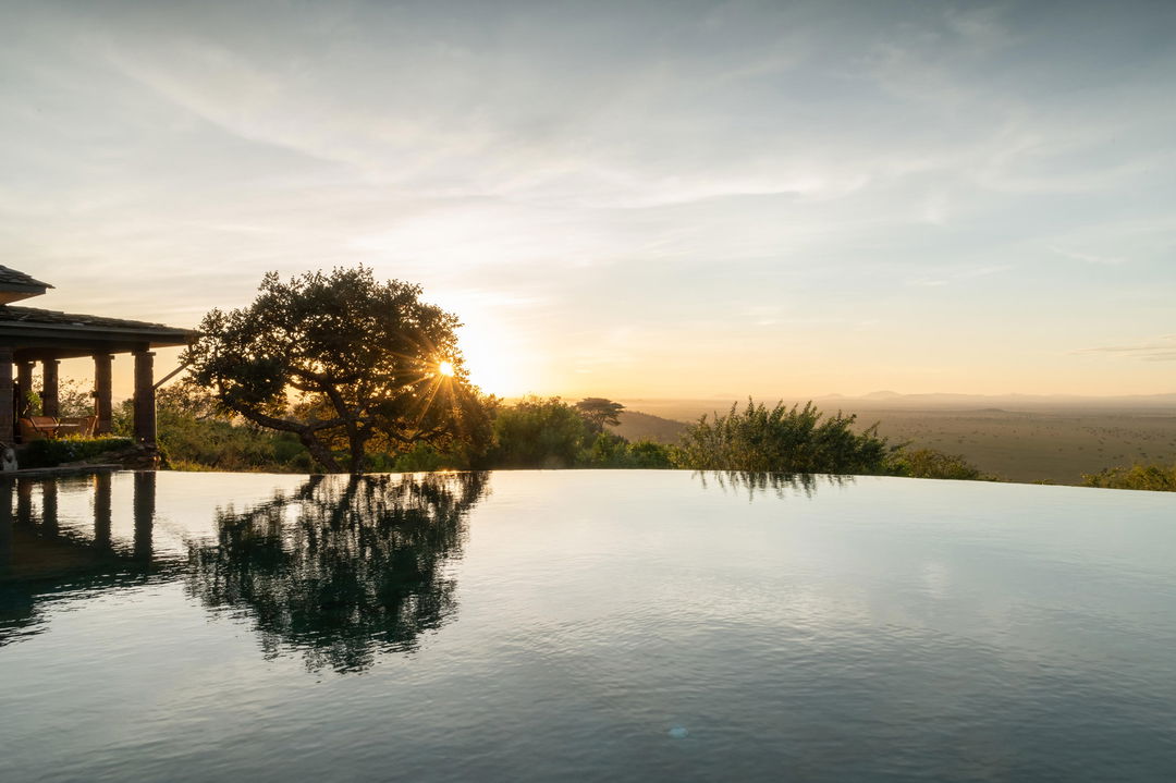 view from the pool at sunset by lady guest in the main rim pool of Singita Sasakwa lodge overlooking the Serengeti