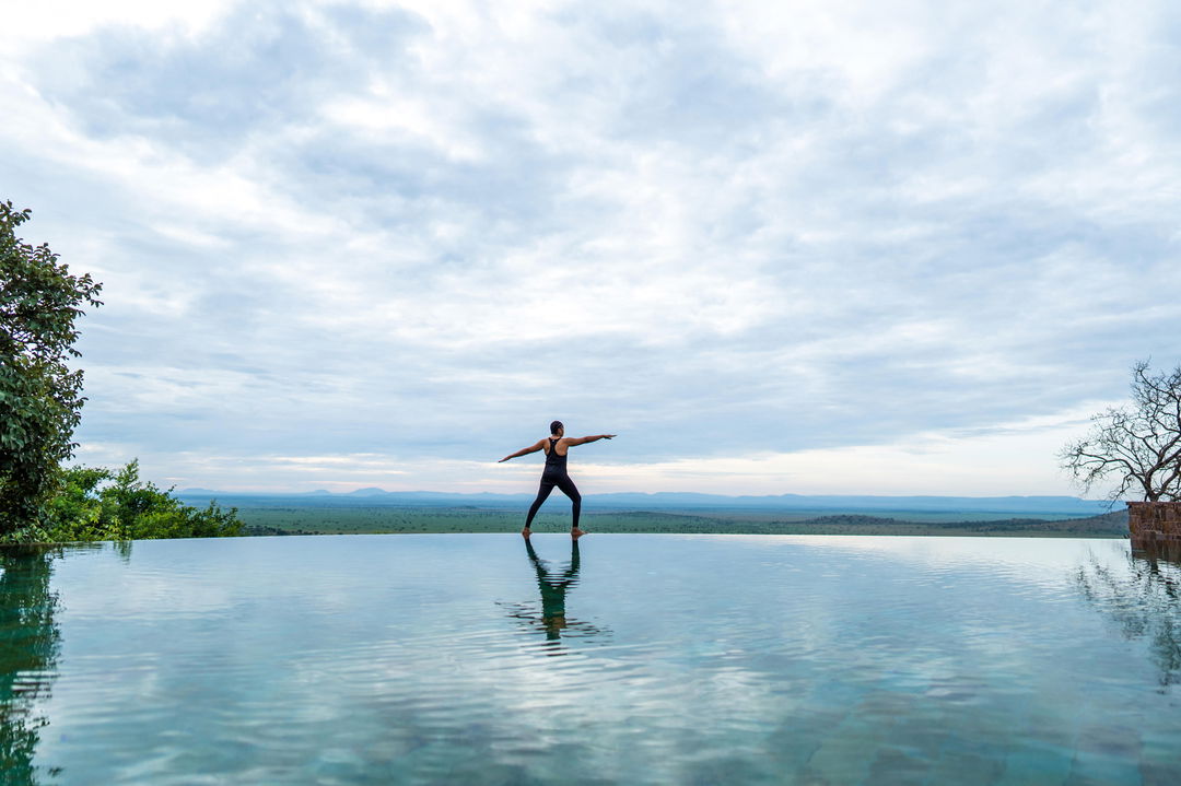 lady guest doing yoga at pool of Singita Sasakwa lodge