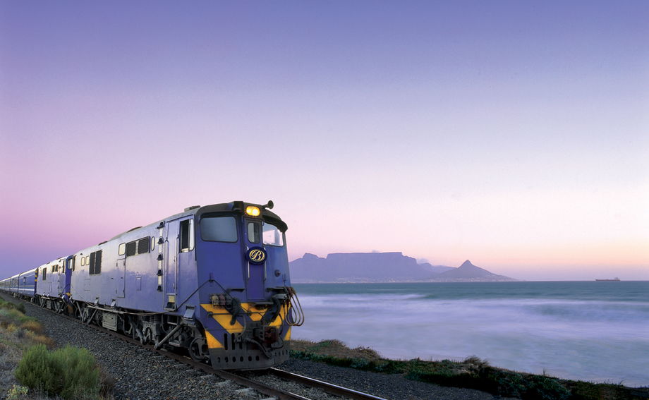blue train on tracks in front of Table mountain cape town