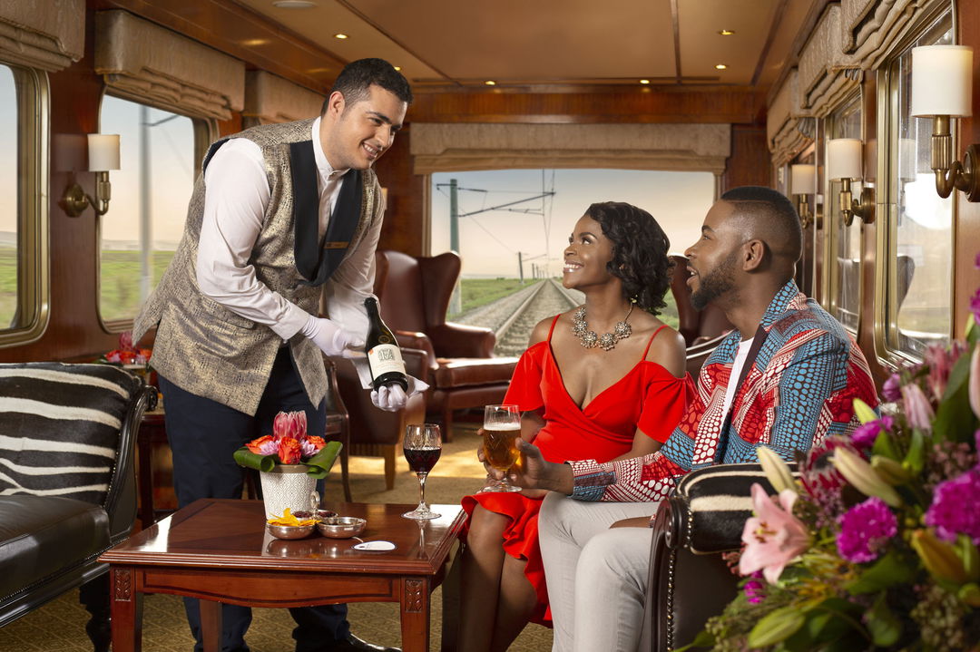 couple served red wine in the observation cart of the blue Train