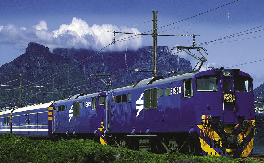 view of blue train on rails in front of table mountain cape town