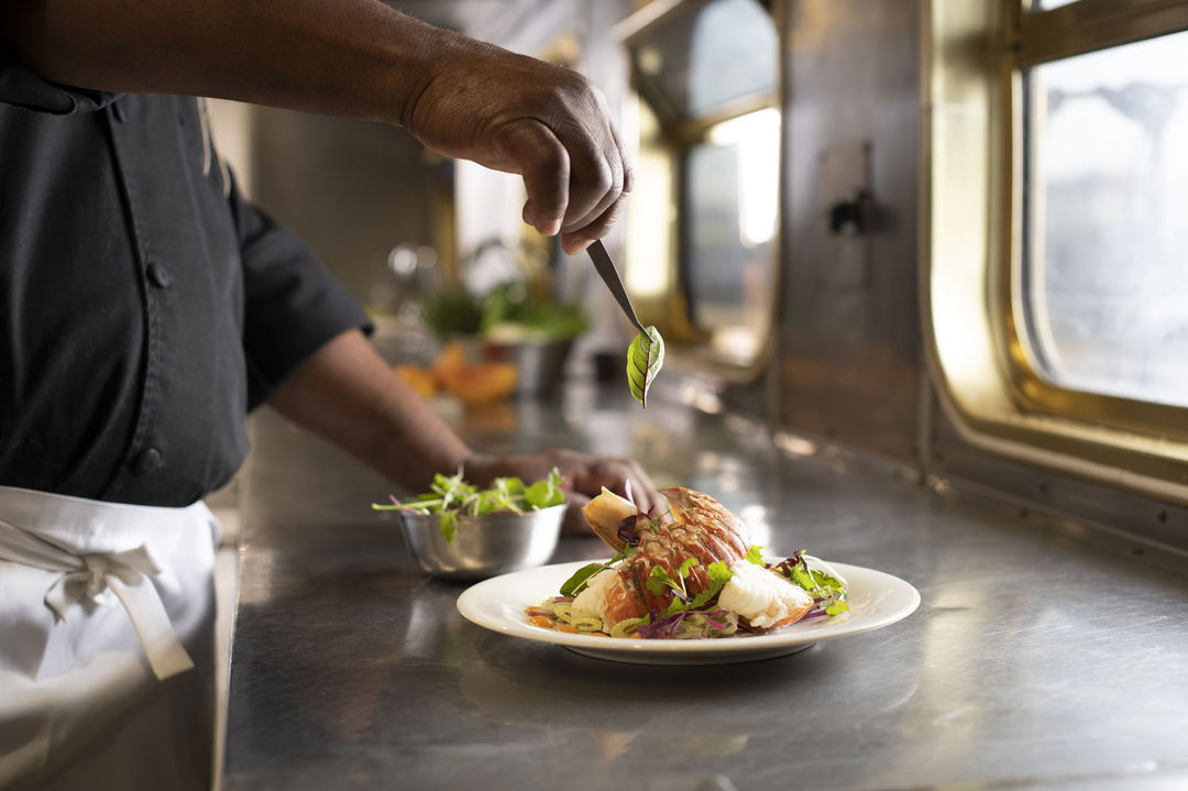 chef decorating a plate with lobster tail on the blue train