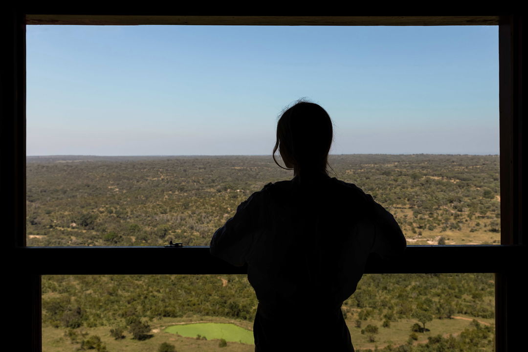 lady guest at ulusaba rock lodge looking out the window at valley below