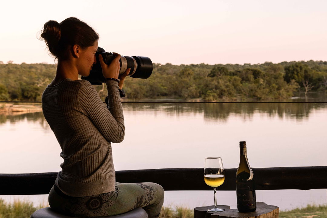 lady guest enjoying wine and photography from deck at dam by Ulusaba lodge