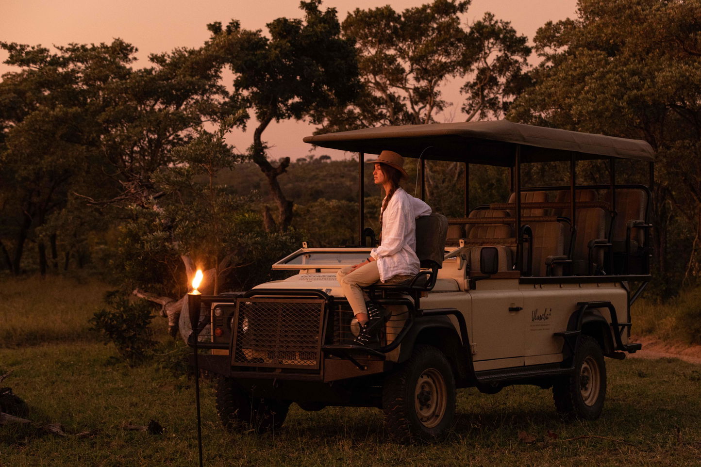 lady guest sitting on hood of safari vehicle in bush with fire in background at Kruger national park