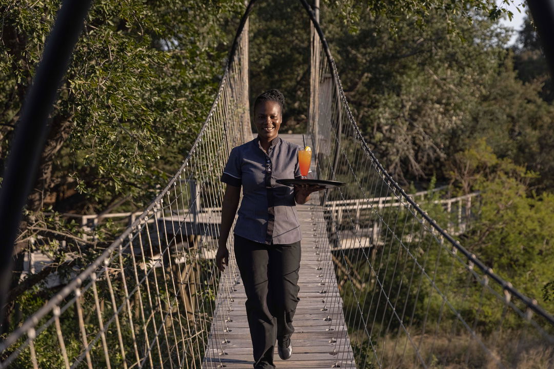waitress with drink tray walking over draw bridge of Ulusaba rock lodge