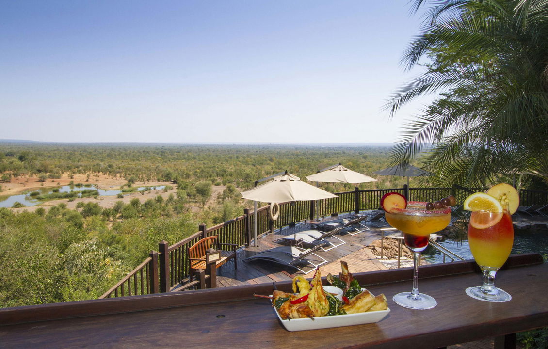 food and cocktail on deck railing with pool below at Victoria falls safari lodge