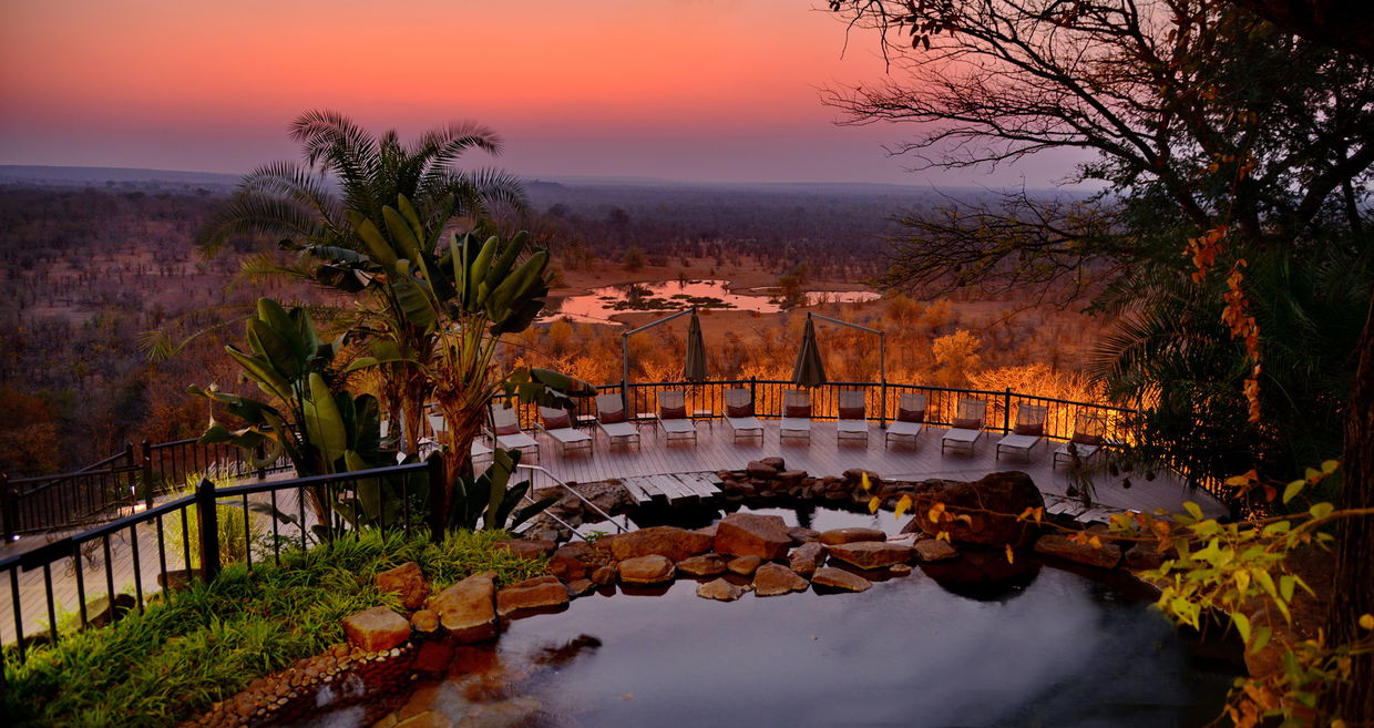 view of pool deck and watering hole at sunset victoria falls safari lodge
