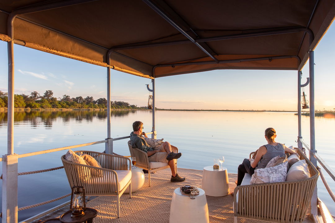 guests with sundowners on barge of wilderness duma tau camp botswana