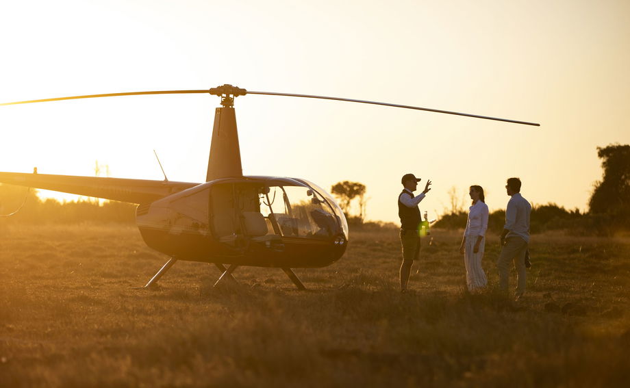 guests with pilot next to grounded helicopter preparing for morning flight at Jao Camp Wilderness Botswana