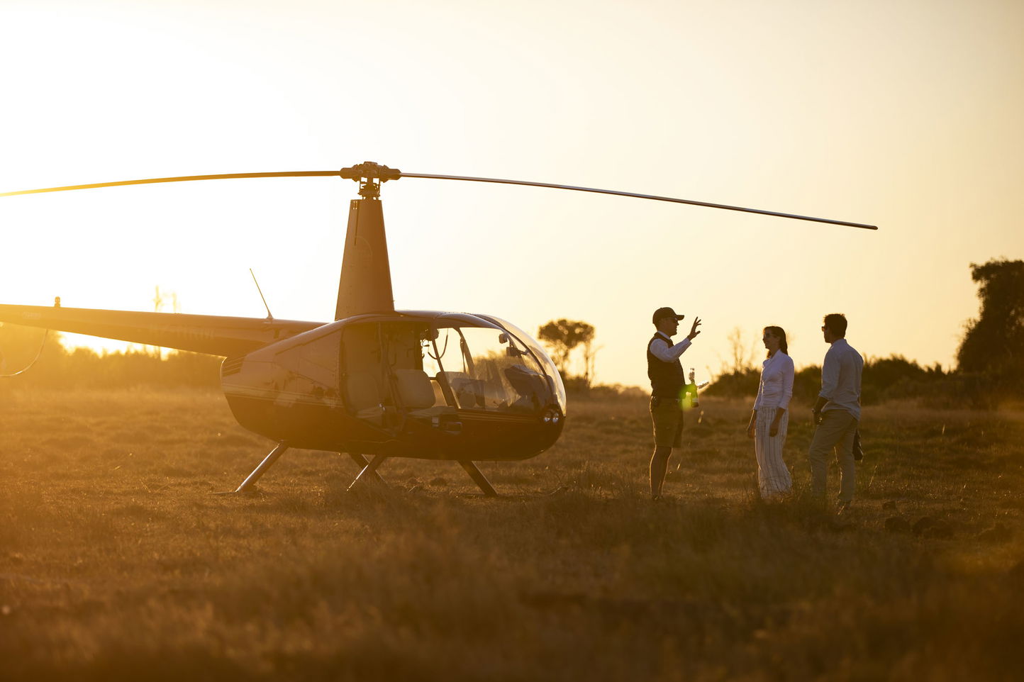 guests with pilot next to grounded helicopter preparing for morning flight at Jao Camp Wilderness Botswana