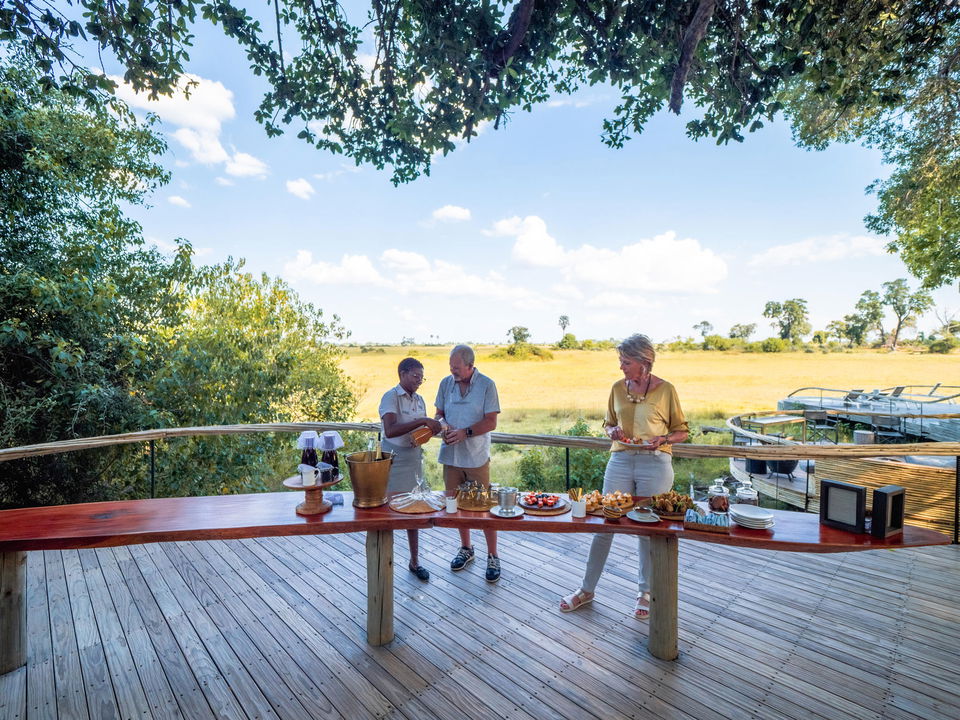 viewing deck with guests having snacks on table with overhanging trees at Okavango Delta by Little Mombo Wilderness
