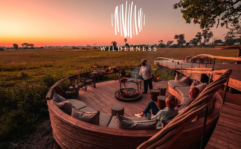 fire pit sunset view of deck and ring couches with staff preparing supper to two guests at Okavango Delta by Little Mombo Wilderness logo overlay fire pit sunset view of deck and ring couches with staff preparing supper to two guests at Okavango Delta by Little Mombo Wilderness logo overlay