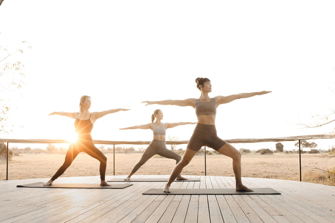 three lady guests doing yoga on viewing deck in the morning at Little Mombo camp Wilderness safaris