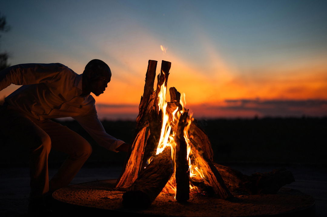 guide stoking a fire at sunset on the Okavango delta at Wilderness Mombo Camp
