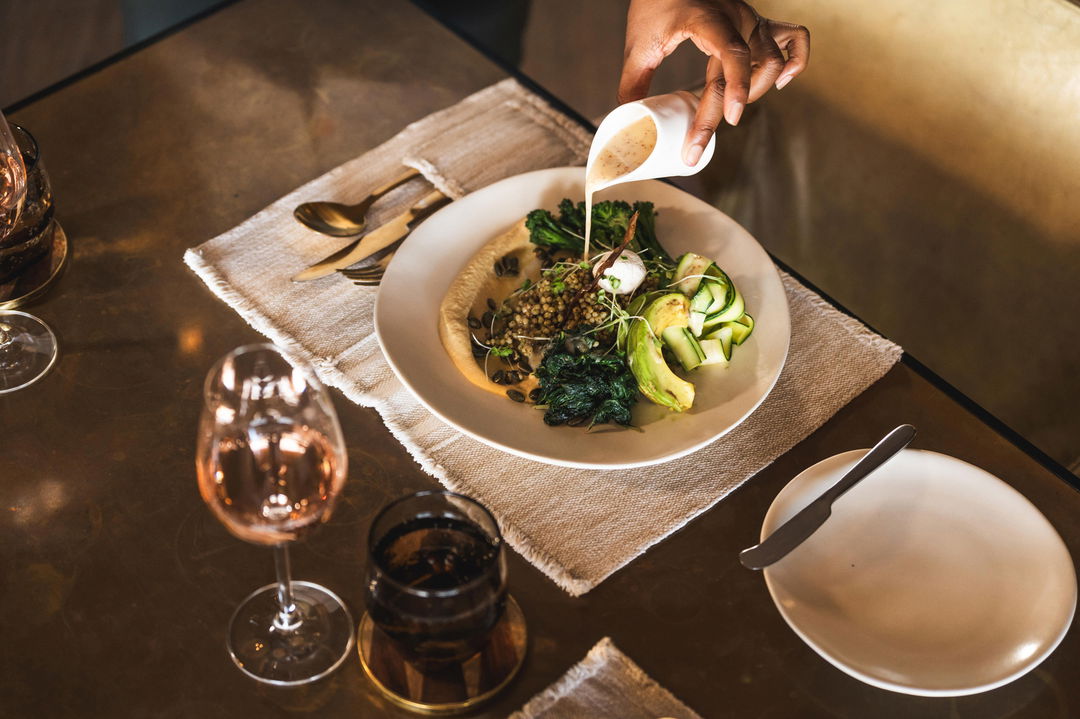 waiter pouring sauce over gourmet food served on table with wine at Wilderness Mombo Camp