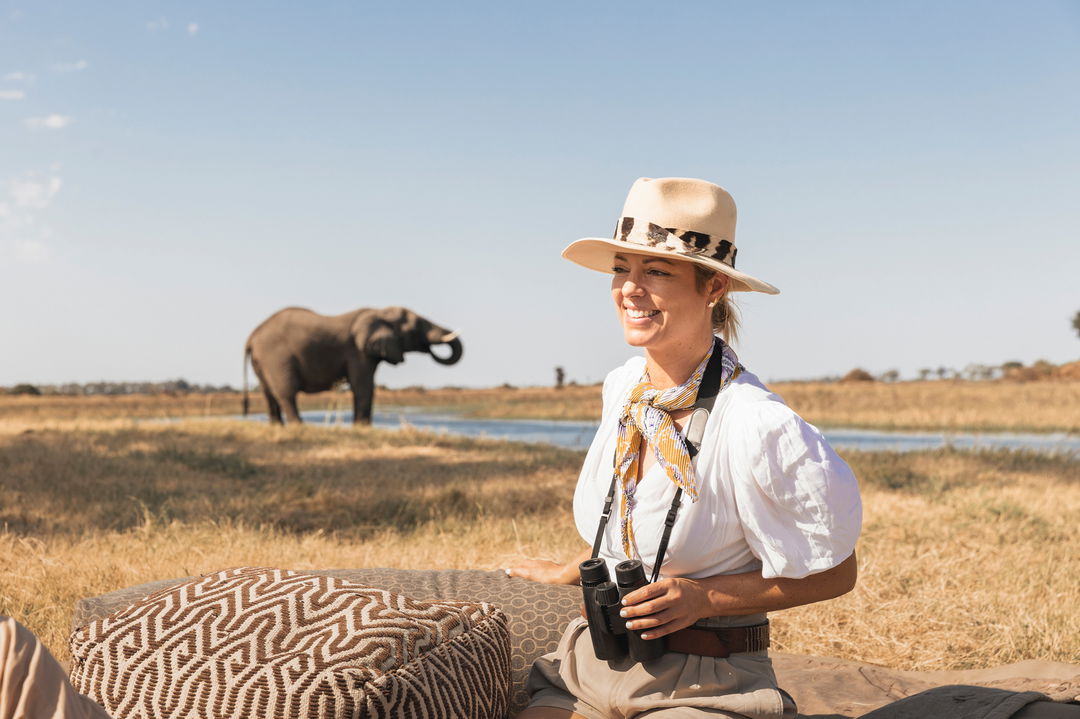  Lady with binoculars in Okavango delta with big elephant in background