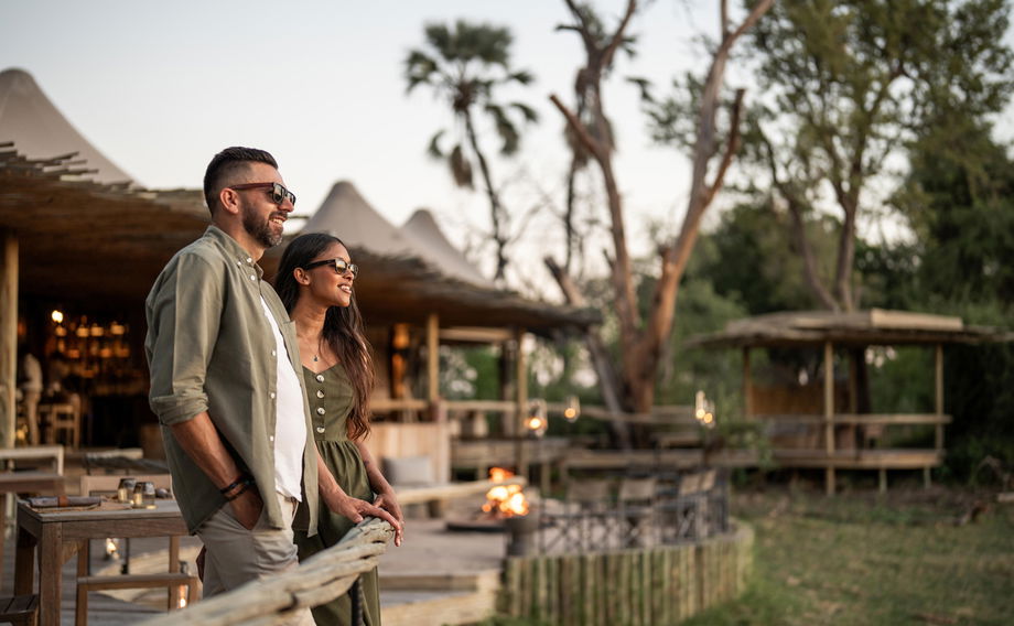 couple on main viewing deck at Wilderness Mombo Camp in Okavango delta with sun setting