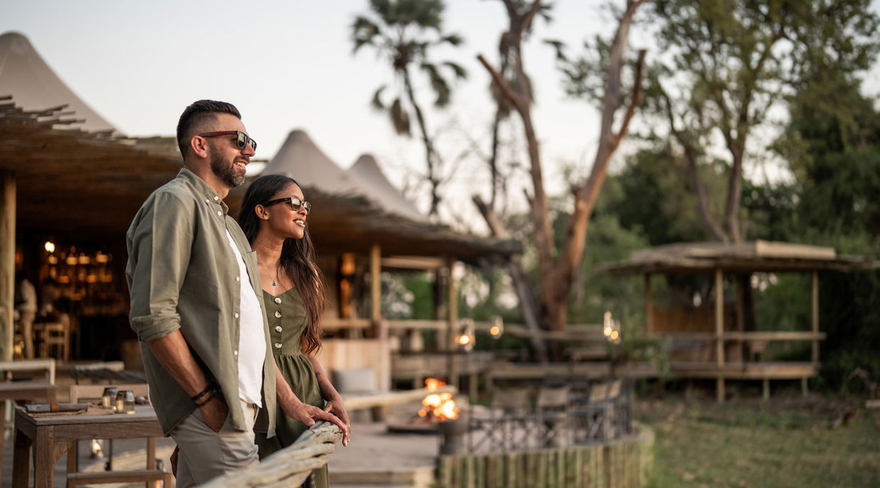 couple on main viewing deck at Wilderness Mombo Camp in Okavango delta with sun setting