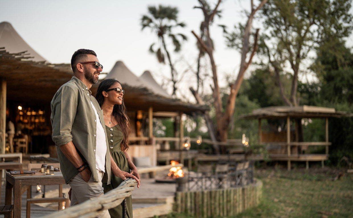 couple on main viewing deck at Wilderness Mombo Camp in Okavango delta with sun setting couple on main viewing deck at Wilderness Mombo Camp in Okavango delta with sun setting