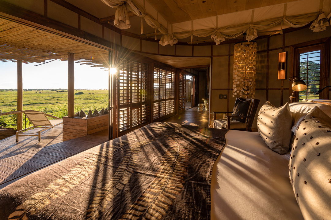 Luxury room with double bed and open doors to view of Okavango delta beyond at Wilderness Mombo Camp