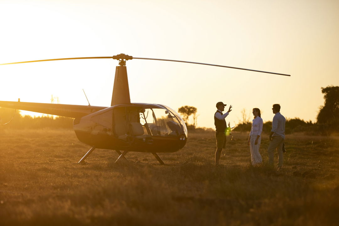 pilot standing in sunset next to helicopter talking to guests in the Okavango delta