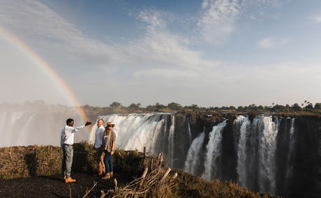 two guests and guide standing at Victoria falls Zimbabwe with rainbow two guests and guide standing at Victoria falls Zimbabwe with rainbow