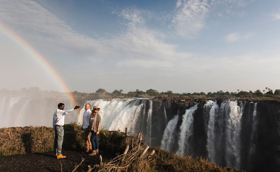 two guests and guide standing at Victoria falls Zimbabwe with rainbow two guests and guide standing at Victoria falls Zimbabwe with rainbow