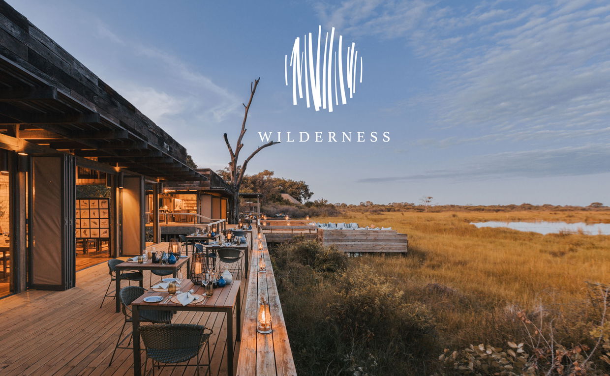 main deck at lodge set up for dinner at sunset at Vumbura Plains Camp Wilderness with logo overlay main deck at lodge set up for dinner at sunset at Vumbura Plains Camp Wilderness with logo overlay