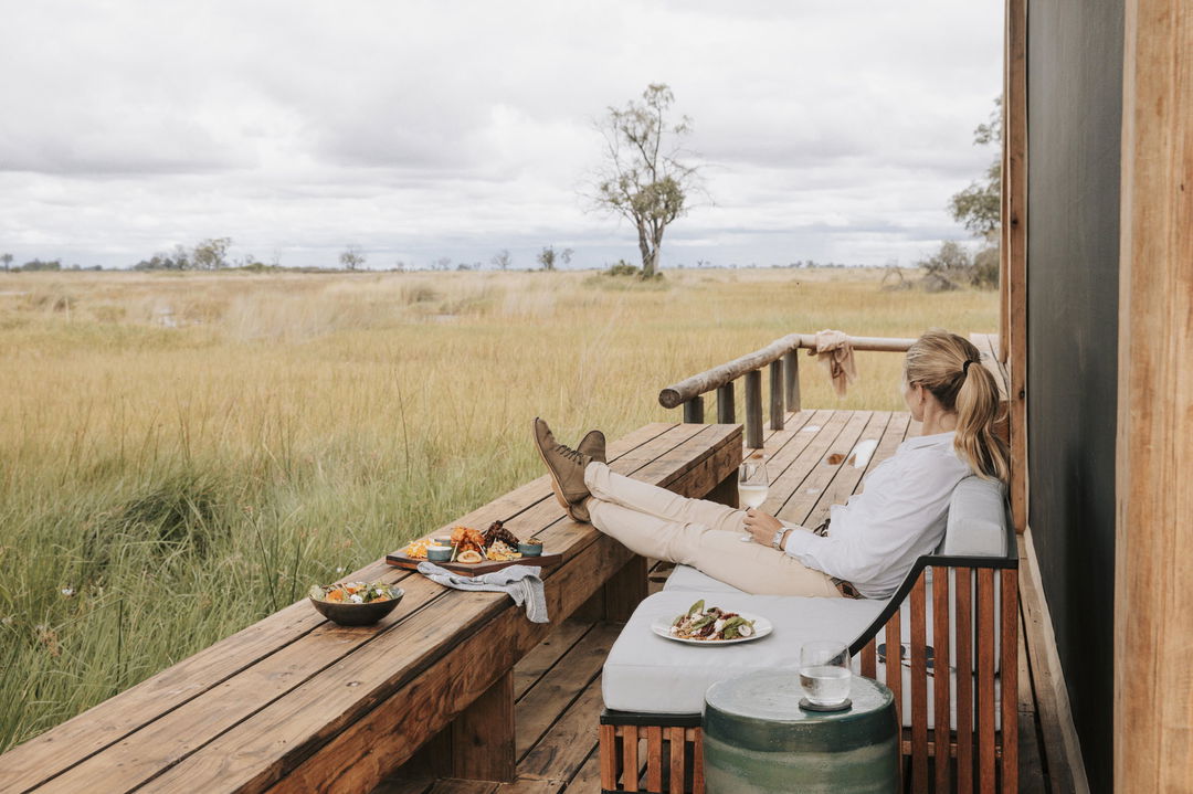 lady guest relaxing on deck of room looking out over delta at Vumbura Plains Camp Wilderness Okavango Delta