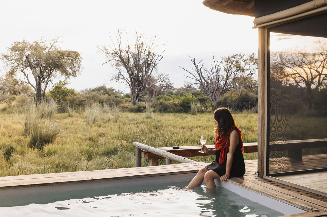 lady with legs dipped in splash pool on deck of room at Vumbura Plains Camp Wilderness Okavango Delta Botswana