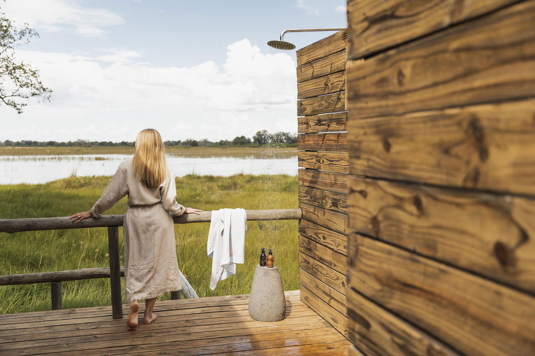 lady guest by outside shower on deck of luxury suite at Vumbura Plains Camp Wilderness Botswana Okavango Delta