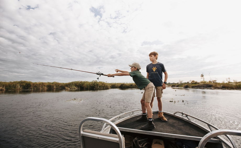two young boys fishing from boat in delta at Vumbura Plains Camp Wilderness Okavango Delta