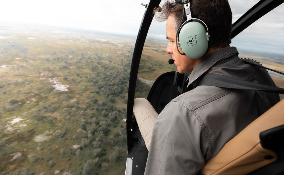 helicopter pilot looking out from flying helicopter at delta below by Vumbura Plains Camp Wilderness Okavango Delta